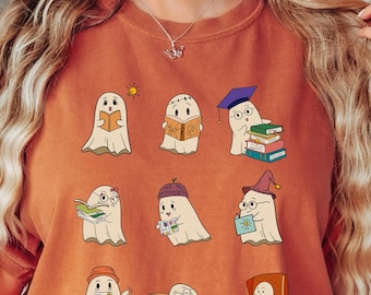 May include: Burnt orange t-shirt featuring a collection of cartoon ghosts reading books. Each ghost is depicted with a unique hat or accessory, such as a graduation cap or glasses. The design is whimsical and book-themed.