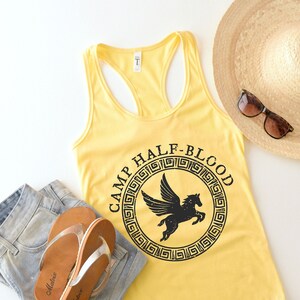 May include: Yellow tank top with a black Camp Half-Blood logo featuring a winged horse. The logo is surrounded by a circle of Greek key patterns.