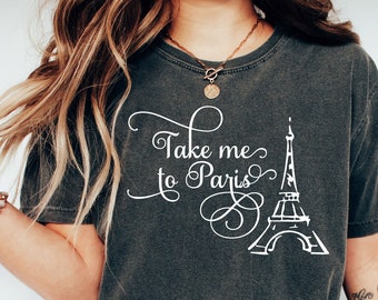 May include: A dark gray t-shirt with the text "Take me to Paris" and a white outline of the Eiffel Tower. The shirt is being worn by a person with long brown hair.