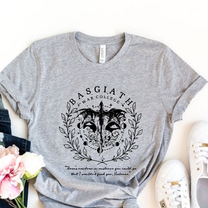 May include: Gray t-shirt with a black graphic design featuring a winged creature, a crescent moon, and the text "Basgiath War College". The text "There's nowhere in existence you could go that I wouldn't find you, Nesta" is printed below the graphic.