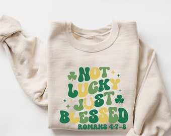 May include: A beige sweatshirt with a green, yellow, and white graphic that reads "Not Lucky Just Blessed Romans 4:7-8".