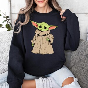 May include: A black sweatshirt with a green and brown cartoon character wearing a brown coat. The character has large ears and is looking to the left.