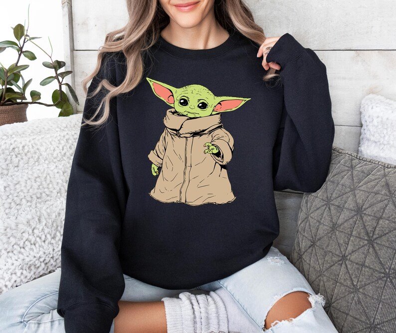 May include: A black sweatshirt with a green and brown cartoon character wearing a brown coat. The character has large ears and is looking to the left.