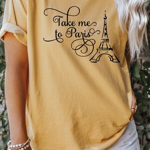 May include: A mustard yellow t-shirt with the text "Take me to Paris" and a black silhouette of the Eiffel Tower.