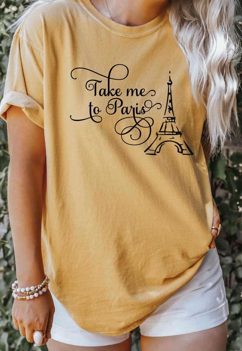 May include: A mustard yellow t-shirt with the text "Take me to Paris" and a black silhouette of the Eiffel Tower.