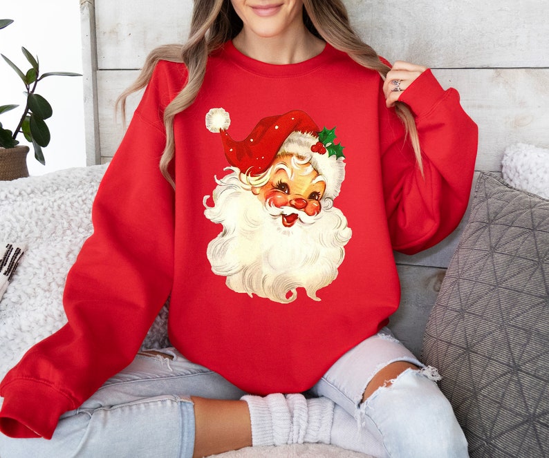 May include: Red Christmas sweatshirt with a vintage illustration of Santa Claus's face. The illustration is in a cartoon style with a white beard and a red hat with white trim.