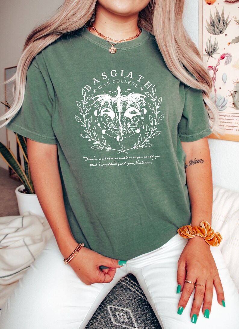 Peut inclure: Un t-shirt vert avec un motif blanc repr&eacute;sentant un dragon, une couronne et le texte "Basgiath War College". Le texte sous le graphique indique "Il n'y a nulle part o&ugrave; vous pourriez aller dans l'existence o&ugrave; je ne vous trouverais pas, Valencas."