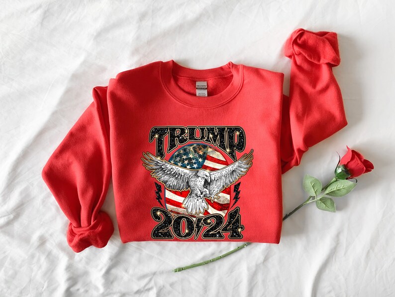 May include: Red sweatshirt with a graphic of an eagle flying over an American flag with the text "TRUMP 2024" in black glitter.
