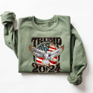 May include: A green sweatshirt with a graphic print of an eagle with an American flag in the background. The text "TRUMP 2024" is printed below the eagle.