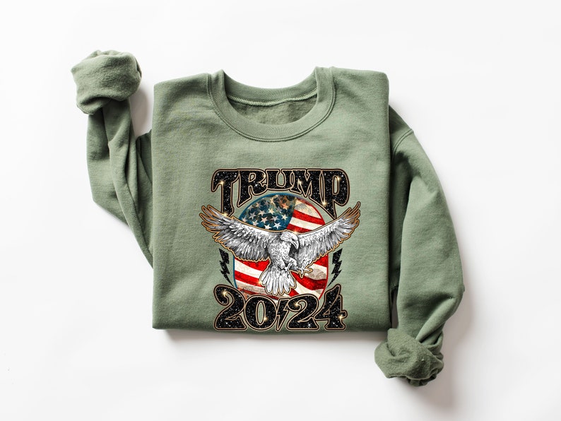 May include: A green sweatshirt with a graphic print of an eagle with an American flag in the background. The text "TRUMP 2024" is printed below the eagle.