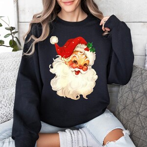 May include: A black sweatshirt with a vintage illustration of Santa Claus's face. Santa is wearing a red hat with white trim and a white beard.