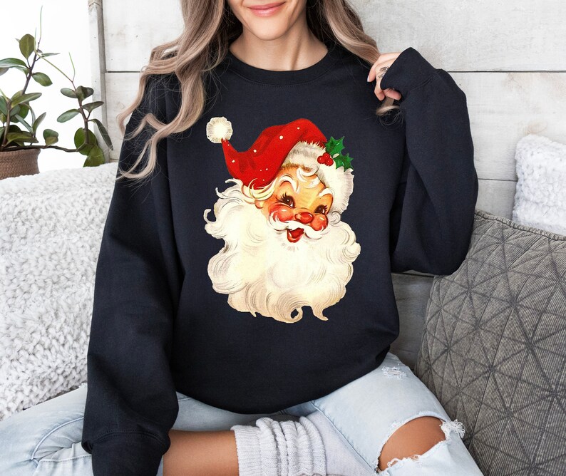 May include: A black sweatshirt with a vintage illustration of Santa Claus's face. Santa is wearing a red hat with white trim and a white beard.