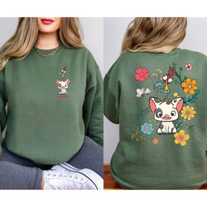 Puede incluir: Una sudadera verde con un dise&ntilde;o de dibujos animados de un cerdo y un gallo. La parte delantera de la sudadera tiene una peque&ntilde;a imagen del cerdo y el gallo, mientras que la parte trasera tiene una imagen m&aacute;s grande con flores y el texto "Moana".