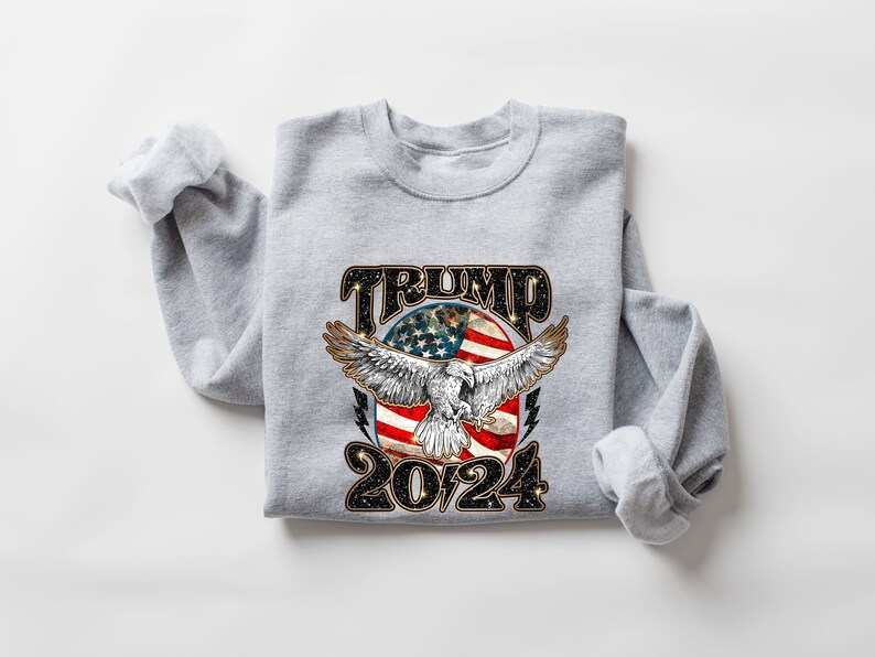 May include: Gray sweatshirt with a graphic of an eagle flying in front of a circle with an American flag and the text "TRUMP 2024".