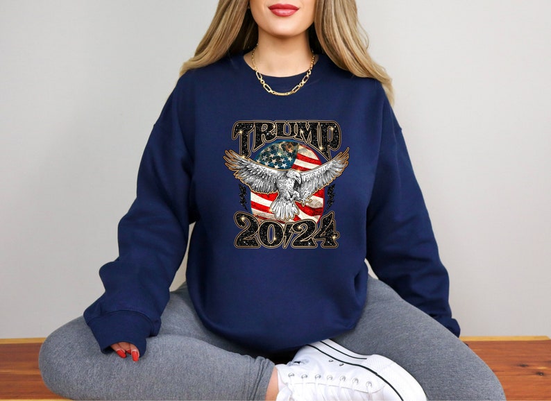 May include: A navy blue sweatshirt with a graphic of an eagle with wings spread, a red, white, and blue American flag, and the text "TRUMP 2024".