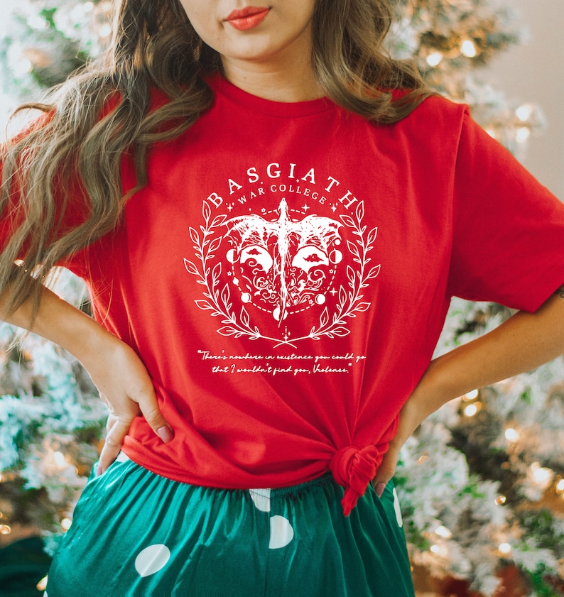 May include: Red t-shirt with a white graphic design featuring a bird with a crown and the text "Basgiath War College". The text "There's nowhere in existence you could go that I wouldn't find you, Volence." is printed below the graphic.