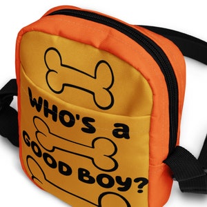 May include: Orange and yellow crossbody bag with a black zipper and strap. The bag has a bone design and the text "Who's a good boy?"