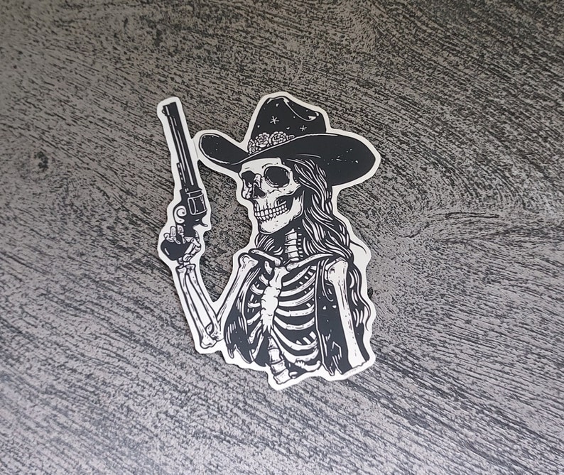Peut inclure: Illustration en noir et blanc d'un squelette portant un chapeau de cowboy et tenant un pistolet. Le squelette porte un gilet et a les cheveux longs.