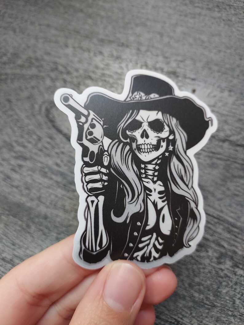 May include: Black and white sticker of a skeleton woman wearing a cowboy hat and holding a gun.
