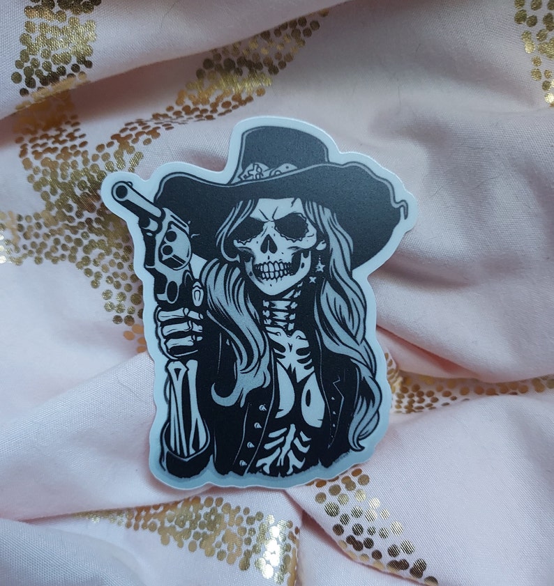 May include: Black and white sticker of a skeleton woman wearing a cowboy hat and holding a gun.