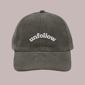 May include: A green corduroy baseball cap with white embroidered text that reads "unfollow" in a retro font.