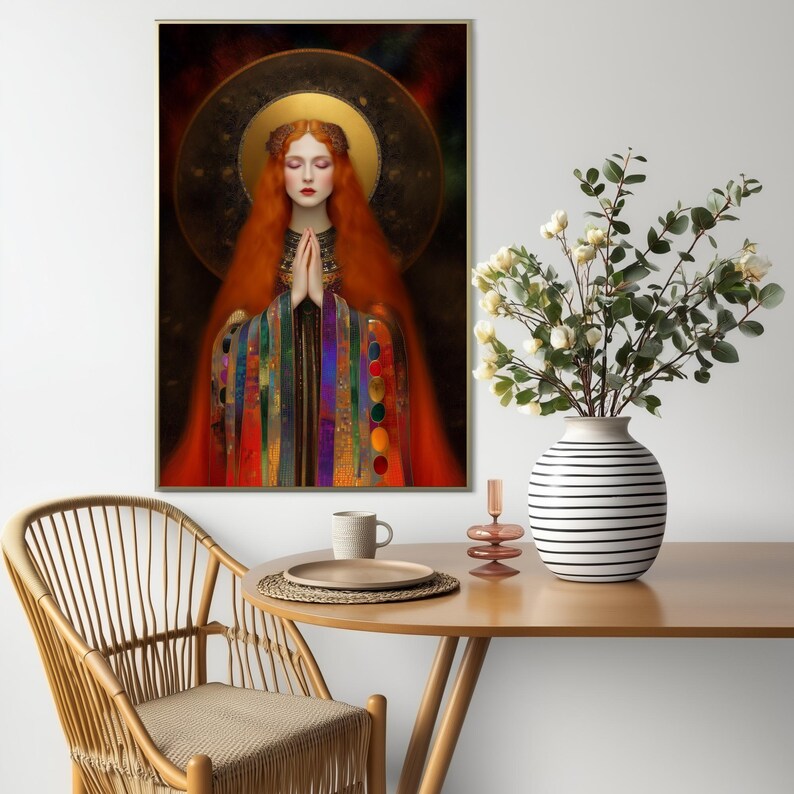 May include: A framed art print depicts a woman with long red hair, a golden halo, and a colorful robe. Her hands are clasped in prayer. The artwork is displayed on a white wall above a wooden table with a vase of flowers.