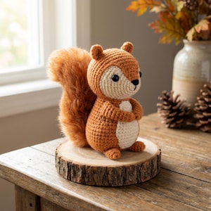 Op de afbeelding: Een handgemaakt gehaakt eekhoornbeeldje in bruin- en crèmetinten, met een pluizige staart. De eekhoorn zit op een kleine, ronde houten schijf. Het beeldje is een charmant decoratief item.