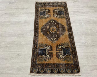 May include: A rectangular area rug featuring a central dark brown diamond medallion on a golden-orange field. The rug includes four dark blue and white geometric corner motifs, a dark brown border with repeating patterns, and short white fringe.