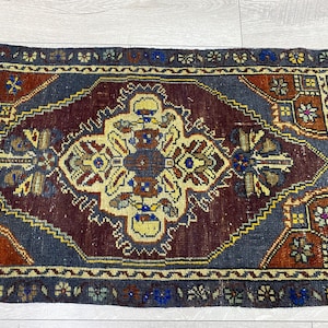 May include: A rectangular area rug featuring a central cream-colored medallion with geometric and floral motifs on a deep burgundy field. The rug is framed by a dark blue border with intricate yellow, red, and blue patterns throughout the design.