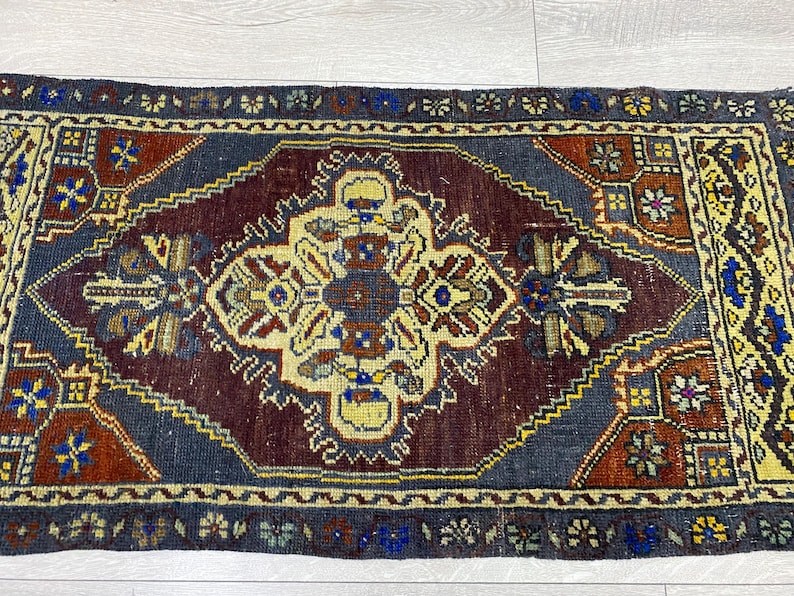 May include: A rectangular area rug featuring a central cream-colored medallion with geometric and floral motifs on a deep burgundy field. The rug is framed by a dark blue border with intricate yellow, red, and blue patterns throughout the design.