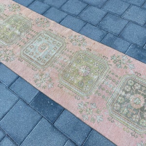 May include: A vintage runner rug with a pink background and green floral patterns. The rug has a distressed look and is perfect for adding a touch of bohemian style to your home.