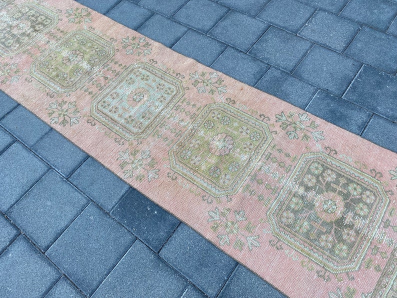 May include: A vintage runner rug with a pink background and green floral patterns. The rug has a distressed look and is perfect for adding a touch of bohemian style to your home.