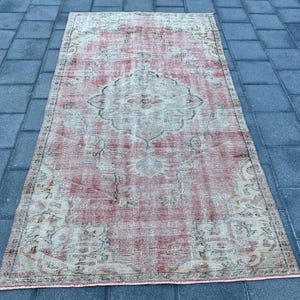 May include: A vintage distressed rug with a faded pink and cream color scheme. The rug features a floral pattern with a central medallion.