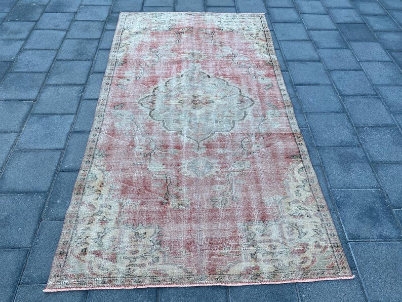May include: A vintage distressed rug with a faded pink and cream color scheme. The rug features a floral pattern with a central medallion.