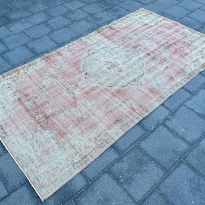 May include: A vintage rug with a faded pink and cream color scheme. The rug has a floral pattern with a central medallion. The rug is worn and has a distressed look.
