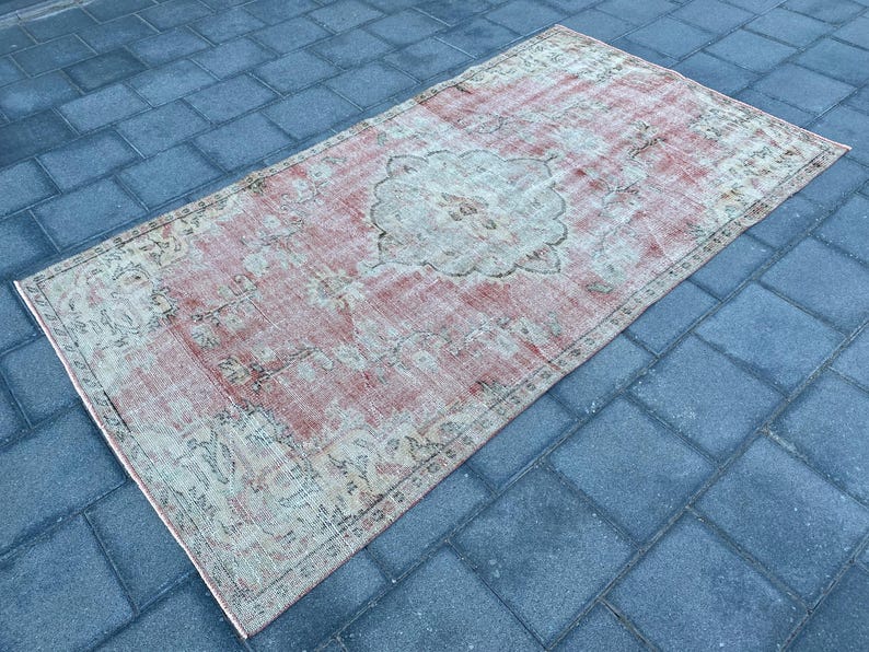 May include: A vintage rug with a faded pink and cream color scheme. The rug has a floral pattern with a central medallion. The rug is worn and has a distressed look.