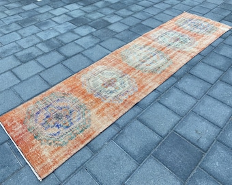 May include: A long, rectangular rug with an orange background and intricate blue, green, and white patterns. The rug has a distressed, vintage look.