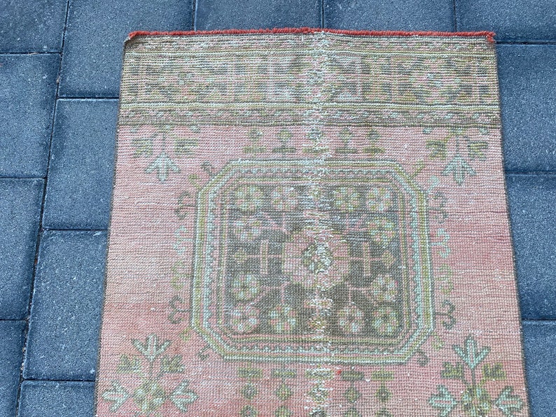 May include: A pink and cream vintage rug with a geometric pattern in the center. The rug has a faded, distressed look and is made of a soft, woven material.