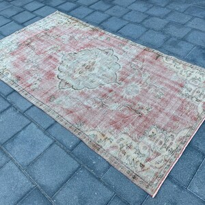 May include: A vintage-style rug with a faded pink background and intricate floral patterns in beige and cream. The rug has a distressed look, adding to its charm.