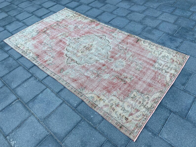 May include: A vintage-style rug with a faded pink background and intricate floral patterns in beige and cream. The rug has a distressed look, adding to its charm.