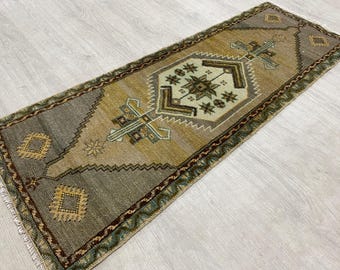 May include: A rectangular area rug featuring a central geometric medallion in cream, surrounded by shades of olive green, mustard yellow, and brown. The border displays intricate patterns with fringe detailing on the short ends.