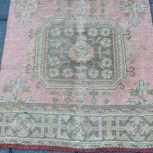 May include: A vintage pink and green rug with a central geometric design. The rug has a faded, distressed look and a fringe border.