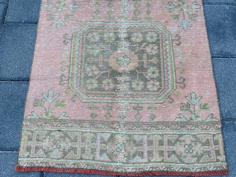 May include: A vintage pink and green rug with a central geometric design. The rug has a faded, distressed look and a fringe border.