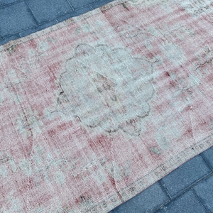 May include: A vintage rug with a faded pink and white color scheme. The rug has a central medallion design with intricate floral patterns. The rug is worn and distressed, giving it a unique and rustic look.