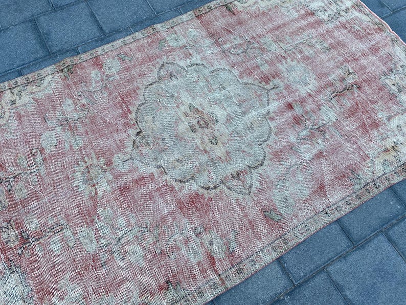 May include: A vintage rug with a faded pink and white color scheme. The rug has a central medallion design with intricate floral patterns. The rug is worn and distressed, giving it a unique and rustic look.