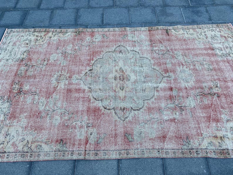May include: A vintage rug with a faded pink and cream color scheme. The rug has a central medallion design with intricate floral patterns.