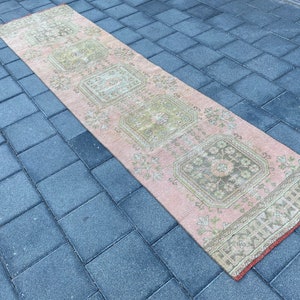 May include: A pink and cream runner rug with a floral pattern. The rug has a distressed look and is made of a soft, woven material.