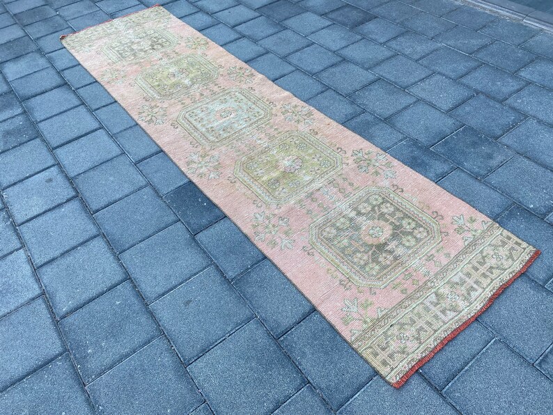 May include: A pink and cream runner rug with a floral pattern. The rug has a distressed look and is made of a soft, woven material.