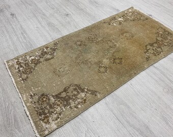 May include: A rectangular area rug featuring a faded tan and beige base with dark brown floral and geometric patterns concentrated at the corners and edges. The rug has a low-pile texture and short white fringe along the two shorter ends.