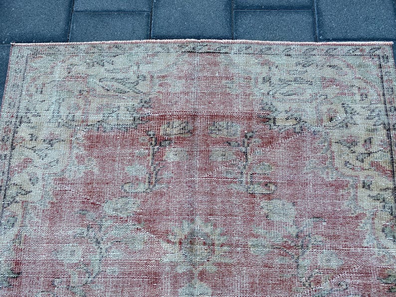 May include: A vintage rug with a faded pink background and a floral pattern in shades of gray and white.